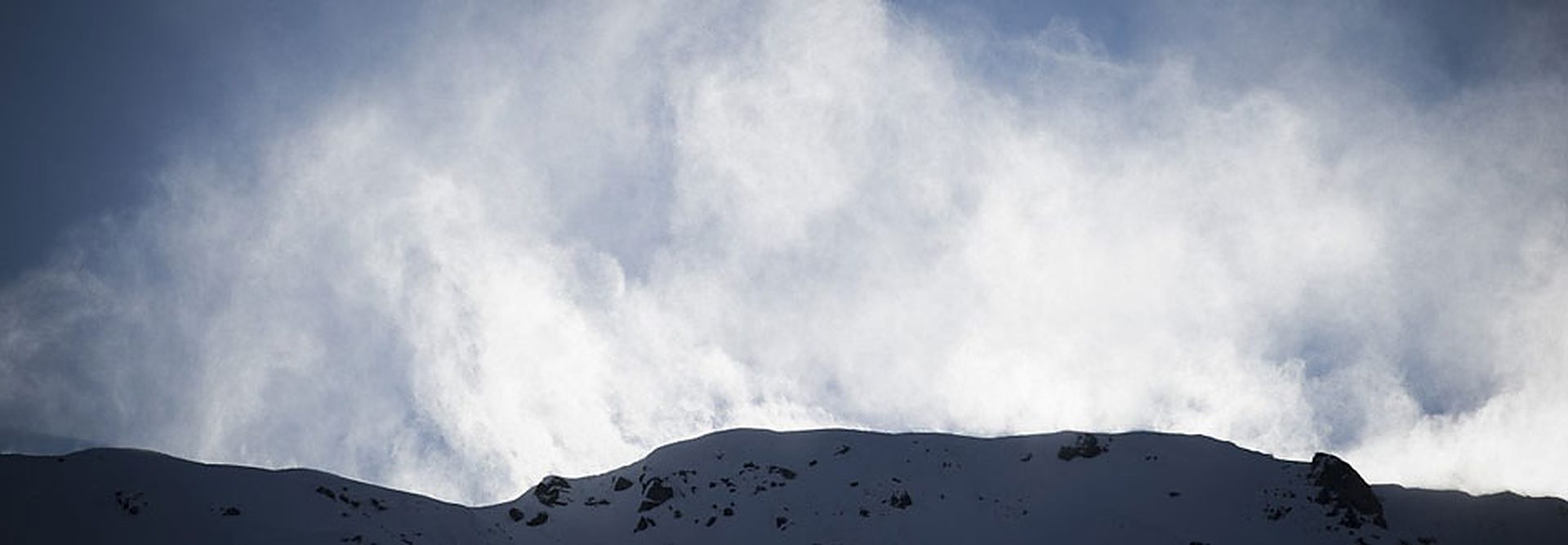 Wind-blown snow drifting off a mountain ridge under a deep blue sky
